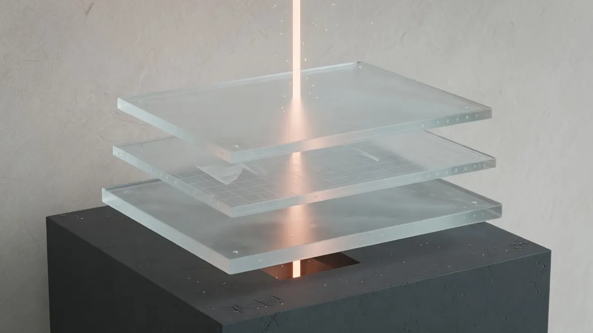 Drei gestapelte Glasscheiben, durch die eine dünne Lichtlinie steigt — Architektur ohne Logos.