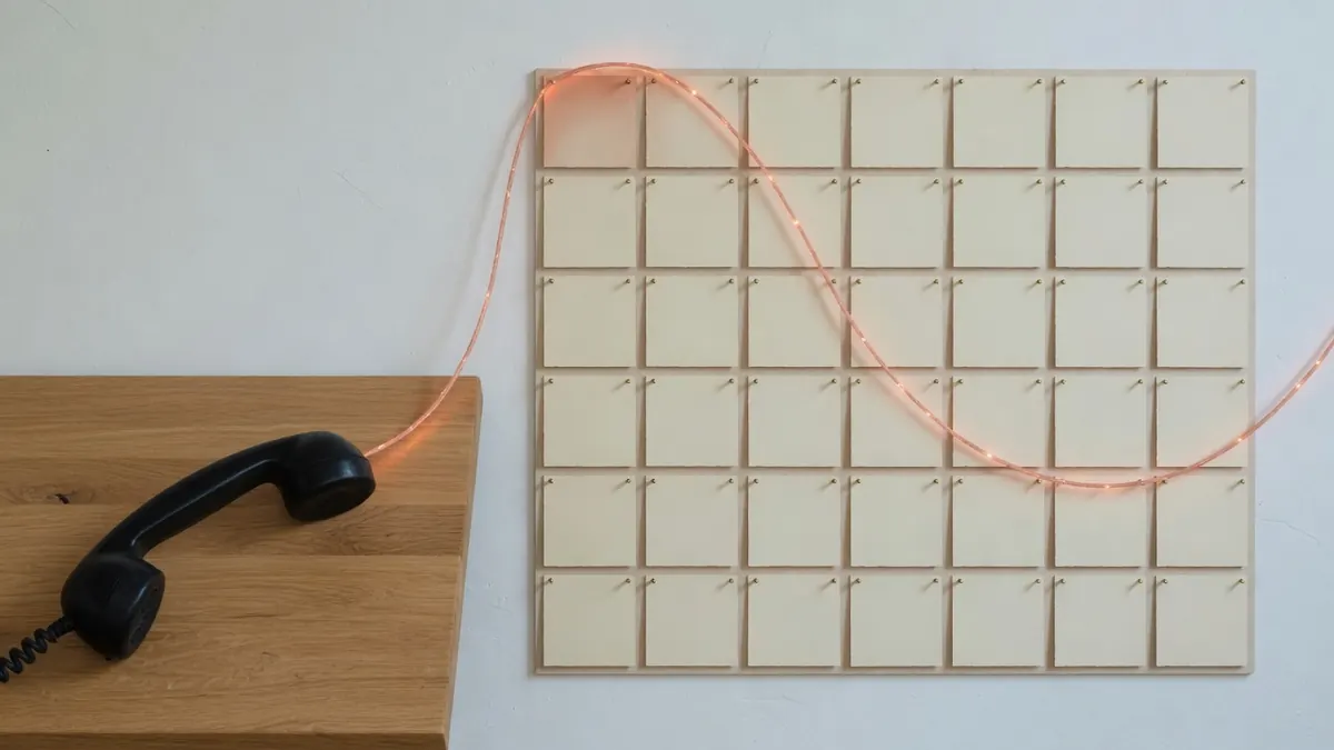 Telefonhörer auf Eiche, verbunden mit einem leeren Kartenraster durch einen dünnen Lichtfaden.